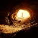 Man standing at entrace of cave looking out.