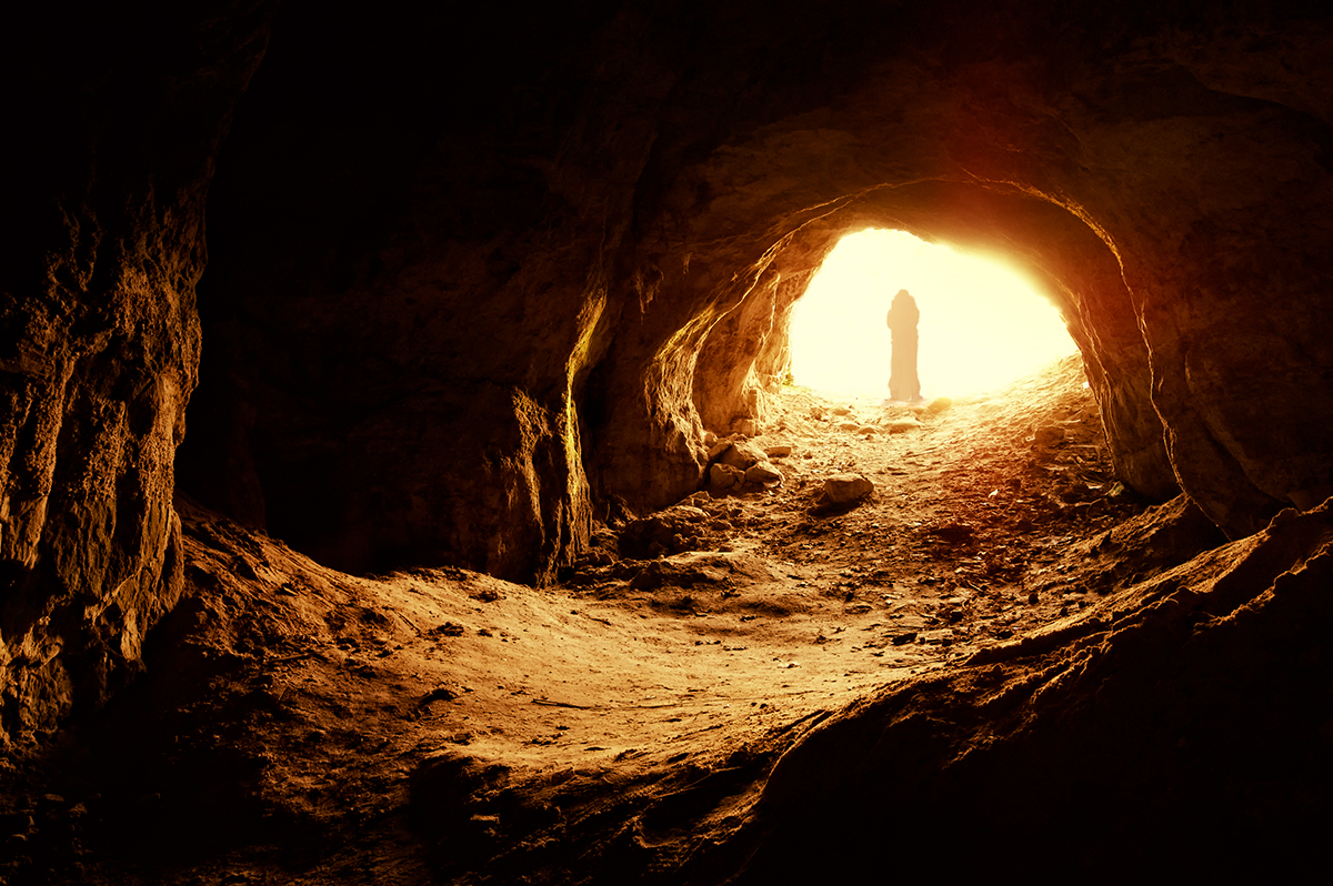 Man standing at entrace of cave looking out.